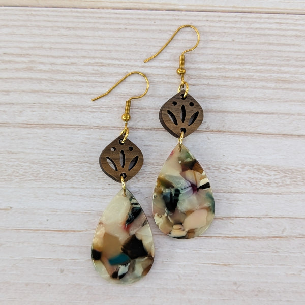 Pair of earrings with teardrop-shaped marbled drops and gold accents on a light wooden surface.