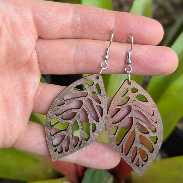 Wooden leaf-shaped earrings with stainless steel hooks held in a hand with a green leafy background