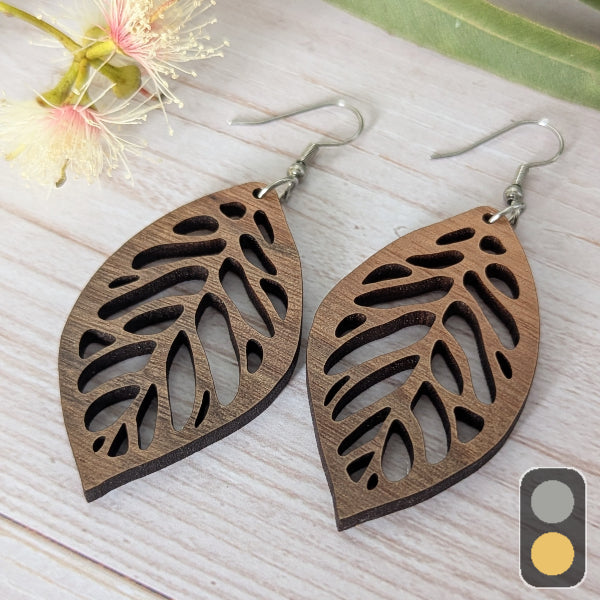 Wooden leaf-shaped earrings on a light wooden surface with a blurred background