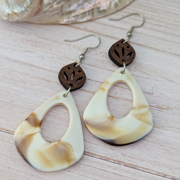 Pair of cream/brown teardrop-shaped earrings with wooden accents on a light wooden surface. Stainless steel hooks.