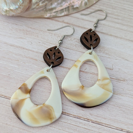 Pair of cream/brown teardrop-shaped earrings with wooden accents on a light wooden surface. Stainless steel hooks.