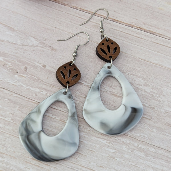 Pair of earrings with marbled grey teardrop shapes and wooden accents on a light wooden surface. Stainless steel hooks.
