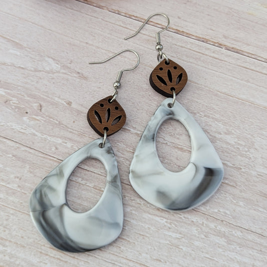 Pair of earrings with marbled grey teardrop shapes and wooden accents on a light wooden surface. Stainless steel hooks.
