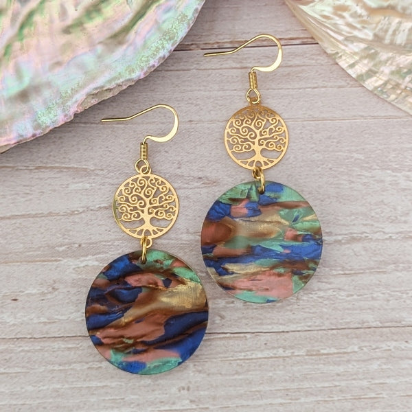 Pair of earrings with gold tree-of-life design and colorful circular pendants on a wooden surface.