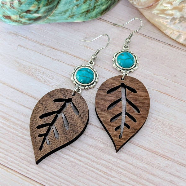 Wooden leaf-shaped earrings with turquoise stones on a light wooden surface.