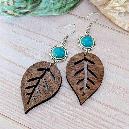 Wooden leaf-shaped earrings with turquoise stones on a light wooden surface.