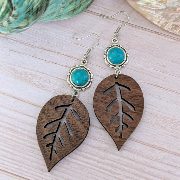 Wooden leaf-shaped earrings with turquoise stones on a light wooden surface
