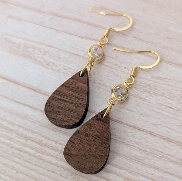 Wooden teardrop earrings with gold and crystal accents on a light wooden surface. Gold plated stainless steel hooks.