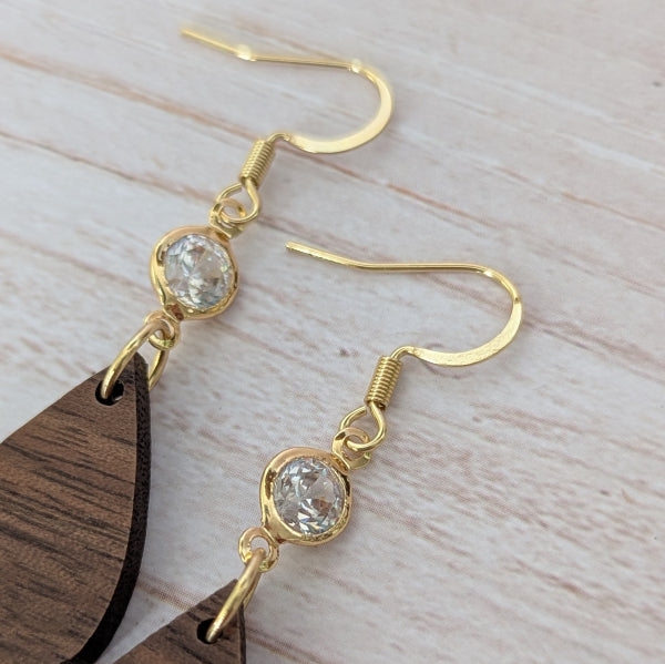 Wooden teardrop earrings with gold and crystal accents on a light wooden surface. Gold plated stainless steel hooks.