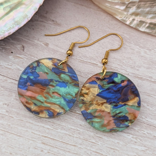 Colorful marbled earrings with gold hooks on a wooden surface.