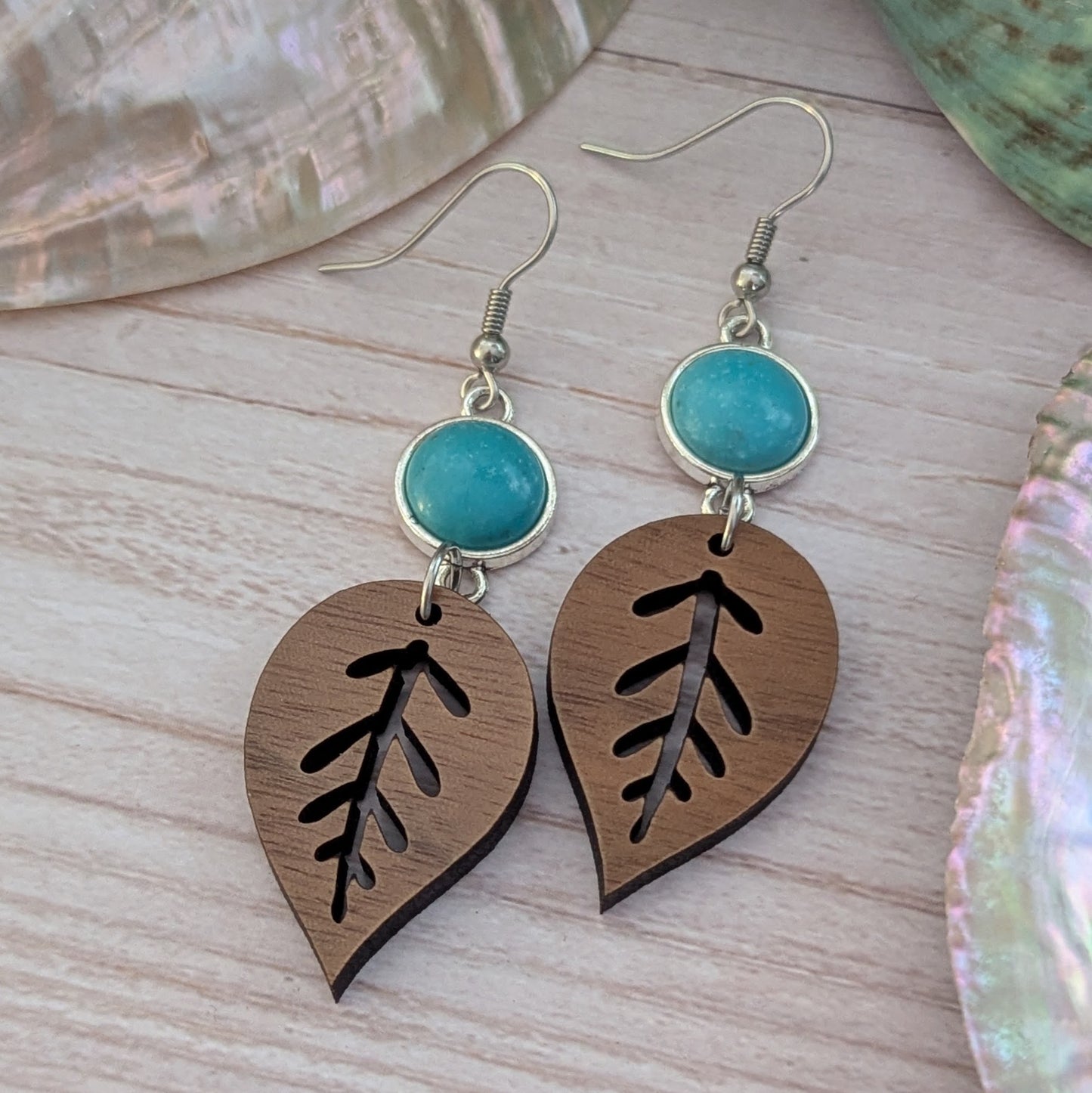 Wooden leaf-shaped earrings with turquoise stones on a wooden surface