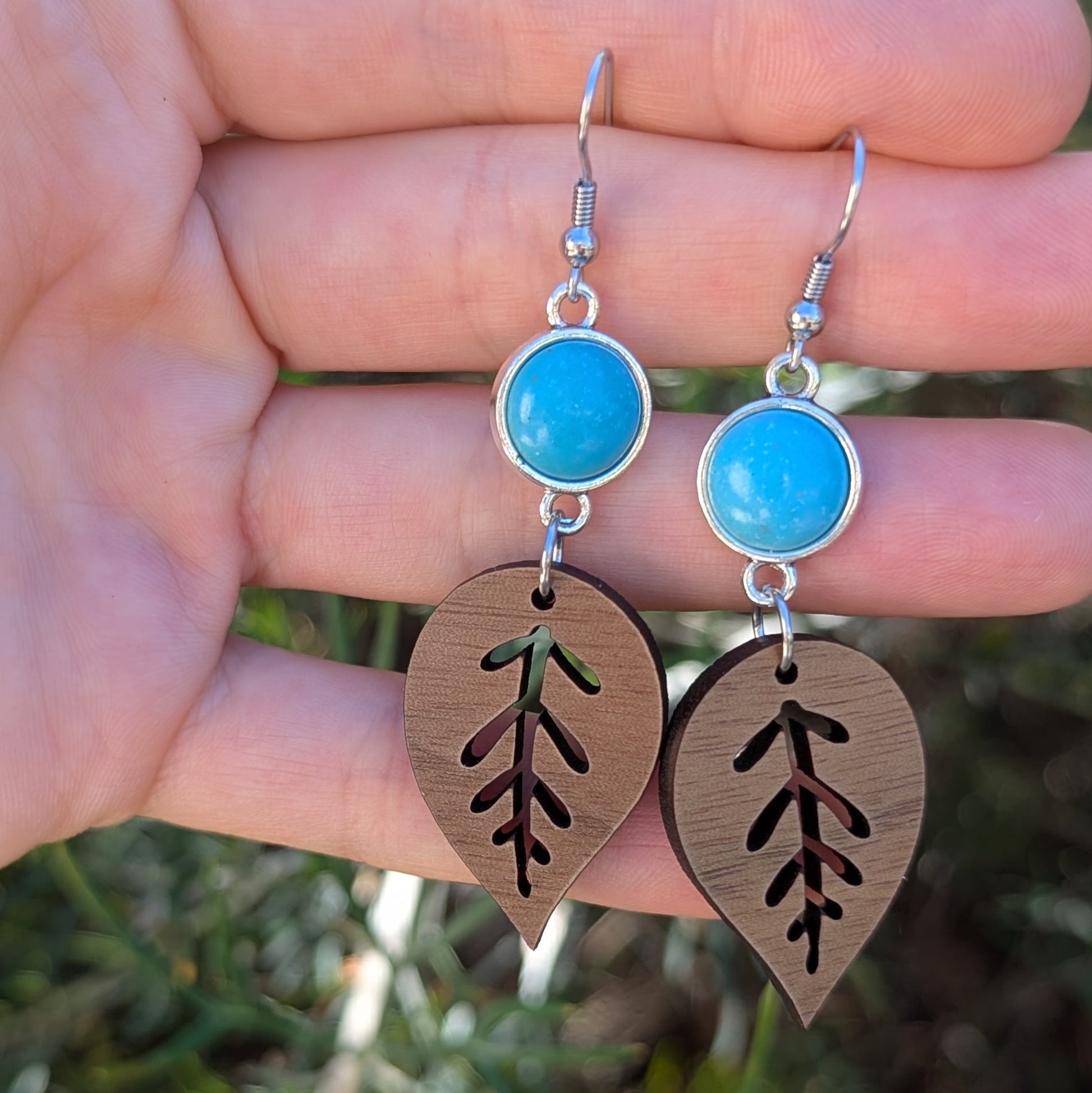 Earrings with turquoise stones and leaf-shaped pendants held in a hand against a natural background.