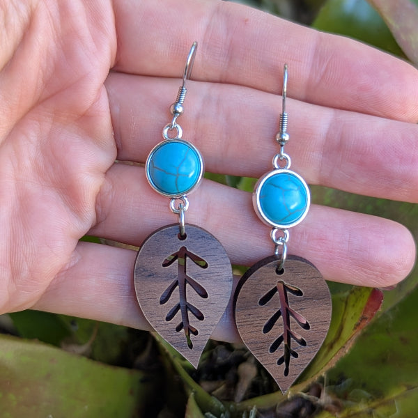 Wooden leaf earrings with turquoise stones held in a hand against a natural background. Stainless steel hooks.