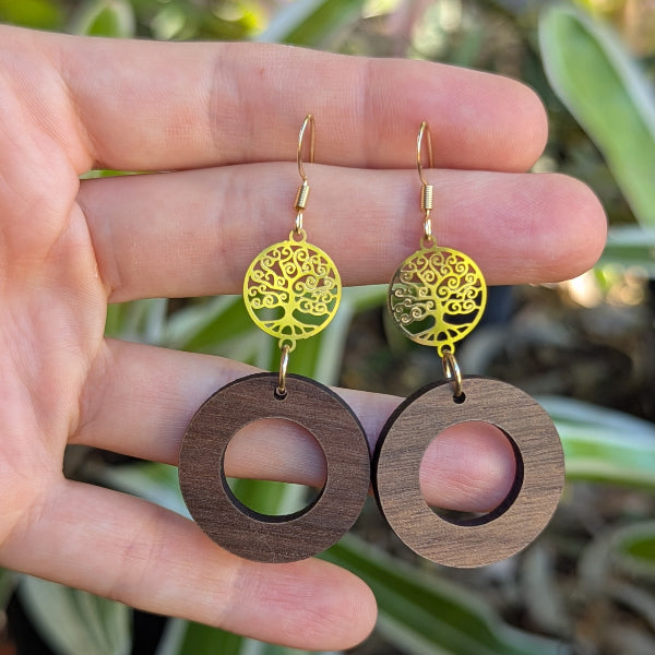 Hand holding a pair of wooden and gold earrings with a natural background