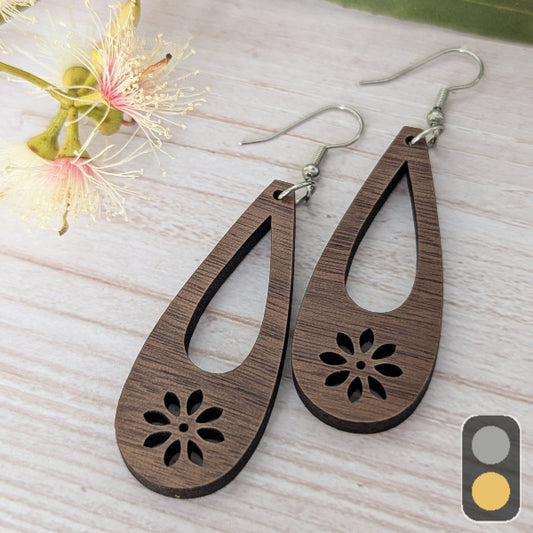 Wooden teardrop earrings with floral cut outs on a light wooden surface with flowers. Stainless steel hooks.