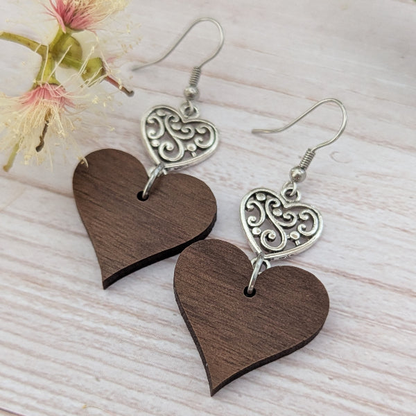 Heart-shaped wooden earrings with silver filigree details on a light wooden surface. Stainless steel hooks.