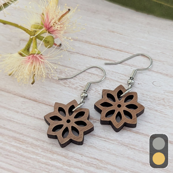 Wooden floral earrings on a light wooden surface with a flower in the background. Stainless steel hooks.