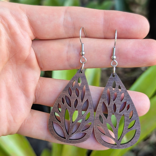 Wooden tear drop earrings held on a with green leaves in the background. Stainless steel hooks.