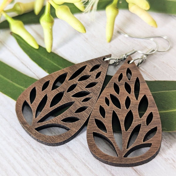Wooden tear drop earrings on a light wooden surface with green leaves in the background. Stainless steel hooks.