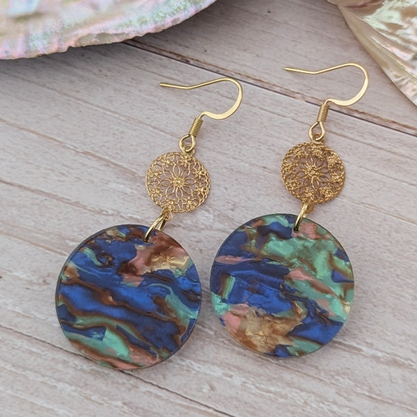 Gold earrings with colorful discs on a wooden surface