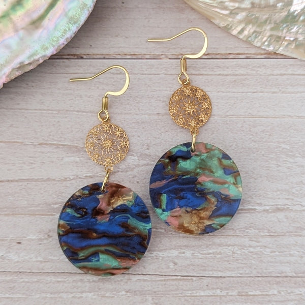Pair of earrings with gold hooks and colorful circular pendants on a wooden surface.