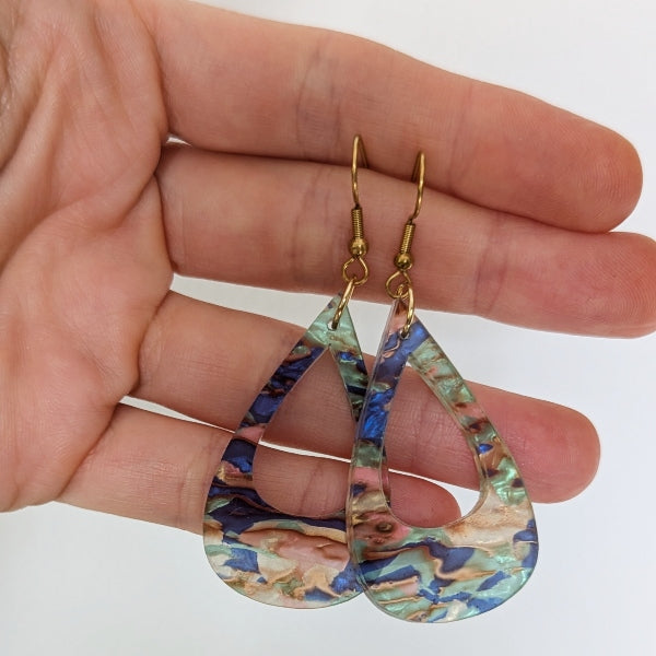 Colorful teardrop-shaped earrings held between fingers against a white background