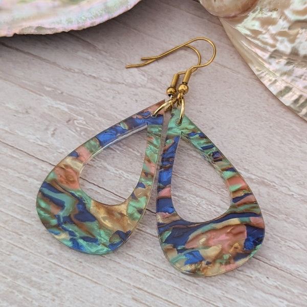 Multicolored teardrop earrings on a wooden surface with seashells in the background.