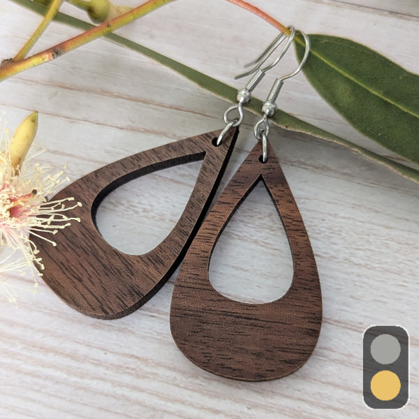Wooden teardrop earrings on a light wooden surface with leaves and flowers. Stainless steel hooks.
