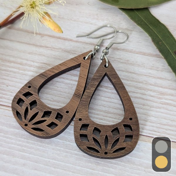 Wooden teardrop-shaped earrings on a light wooden surface with a blurred flower and leaf in the background.