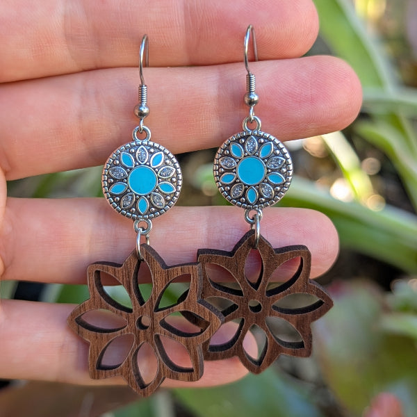 Wooden floral earrings with turquoise coloured enamel on a hand with a green background. Stainless steel hooks.
