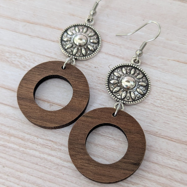 Wooden earrings with silver toned circular designs on a light wooden surface. Stainless steel hooks.