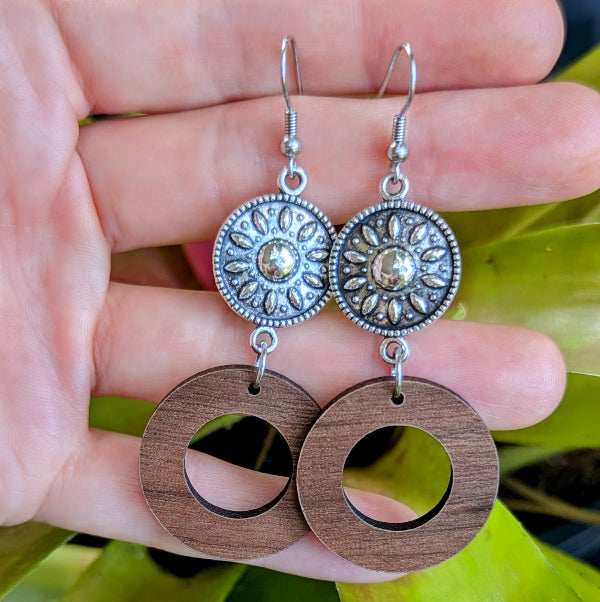 Silver toned and wooden earrings held in a hand with a green leafy background. stainless steel hooks.