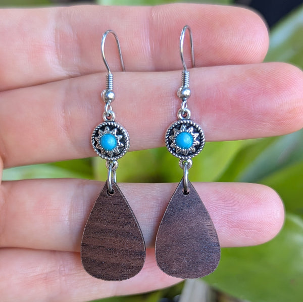 Teardrop earrings with turquoise stones held in a hand against a blurred green background. Stainless steel hooks.