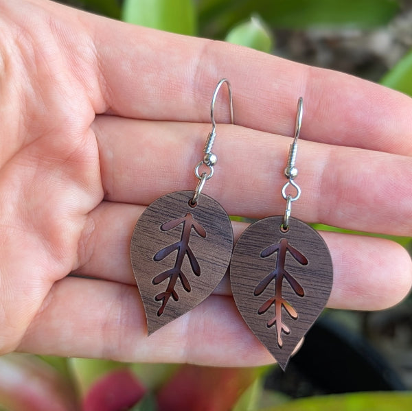 Wooden leaf-shaped earrings held in a hand with a natural background. Stainless steel hooks.