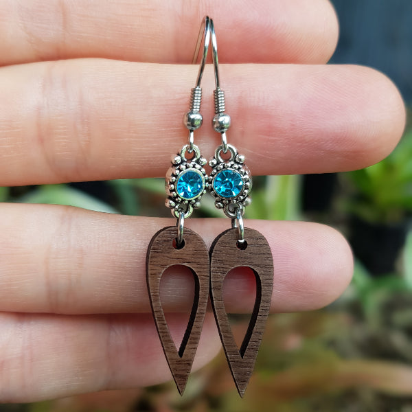 Wooden earrings with blue gemstones held between fingers against a blurred natural background. Stainless steel hooks.