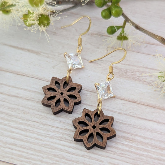 Wooden flower-shaped earrings with gold hooks and clear crystals on a light wooden surface.
