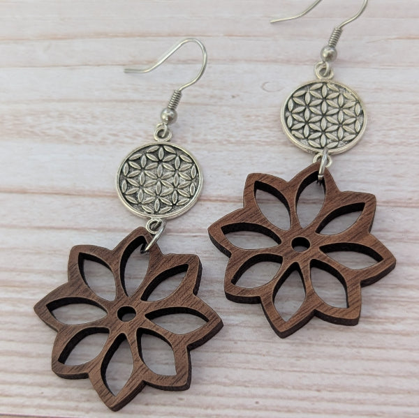 Wooden flower-shaped earrings with silver floral designs on a light wooden surface. Stainless steel hooks.