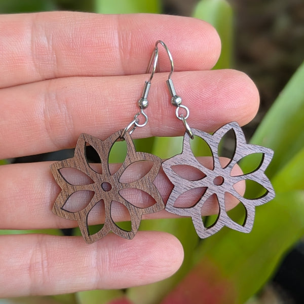 Wooden floral earrings held between fingers with a blurred natural background. Stainless steel hooks.