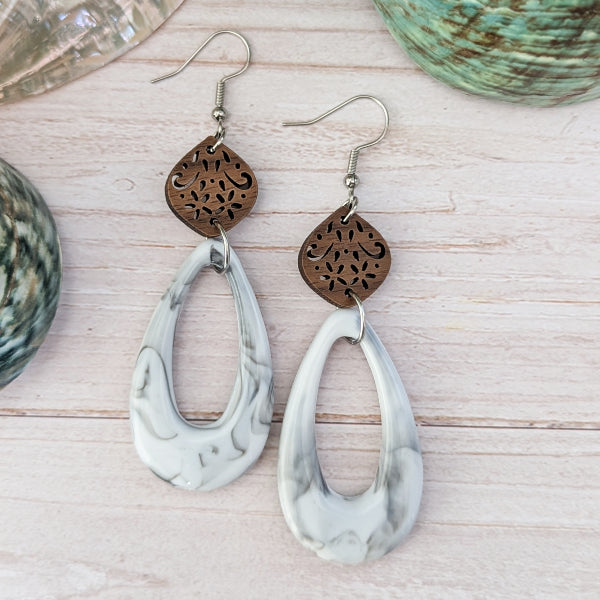 White/grey marble pattern teardrop earrings with wooden floral designs on a wooden surface. Stainless steel hooks.