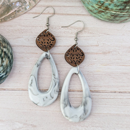 White/grey marble pattern teardrop earrings with wooden floral designs on a wooden surface. Stainless steel hooks.