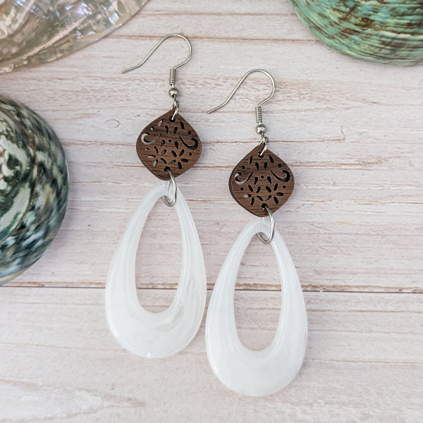 White teardrop earrings with wooden floral designs on a wooden surface. Stainless steel hooks.