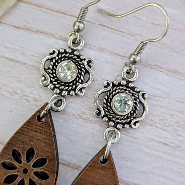 Silver earrings with wooden teardrop pendants on a light wood background