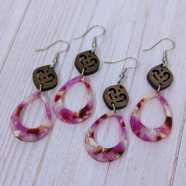 Wooden and pink resin earrings on a pale wood surface.