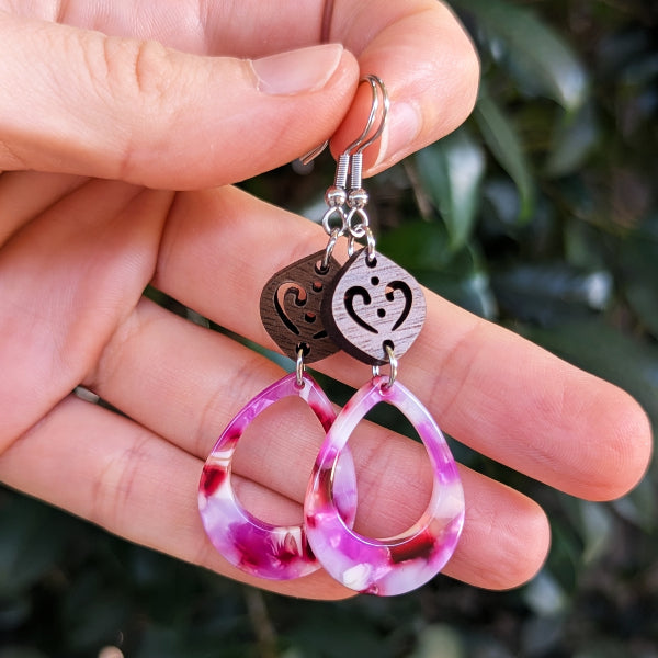 Wooden and pink resin earrings held in a hand.