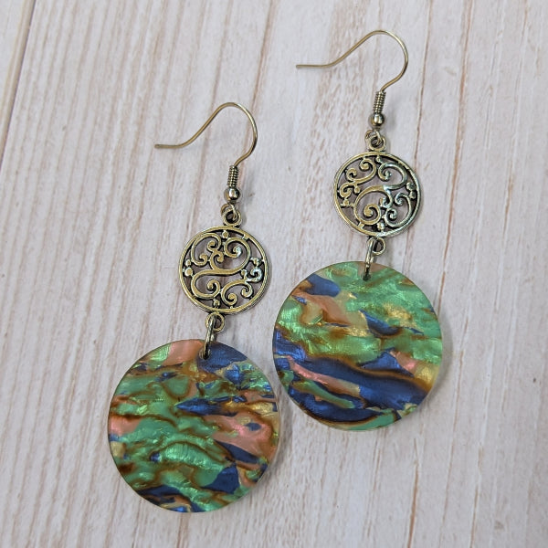 Pair of earrings with colorful circular designs and intricate stainless steel hooks on a wooden surface.