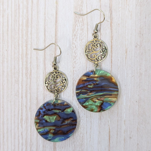 Pair of earrings with circular multicolored discs on a light wooden background.