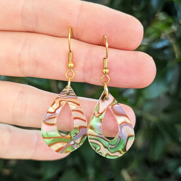 Multi coloured acrylic tear drops with gold toned hooks, against a green blurred background.