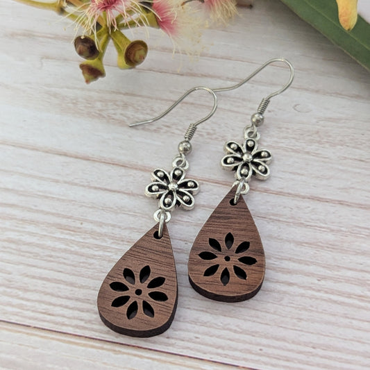 Wooden teardrop earrings with silver toned floral designs on a light wooden surface. Stainless steel hooks.