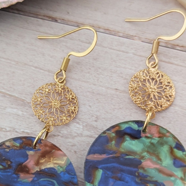Gold earrings with intricate designs and colorful dangling elements on a wooden surface.