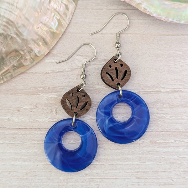 Pair of blue circular earrings with wooden accents on a light wood surface.